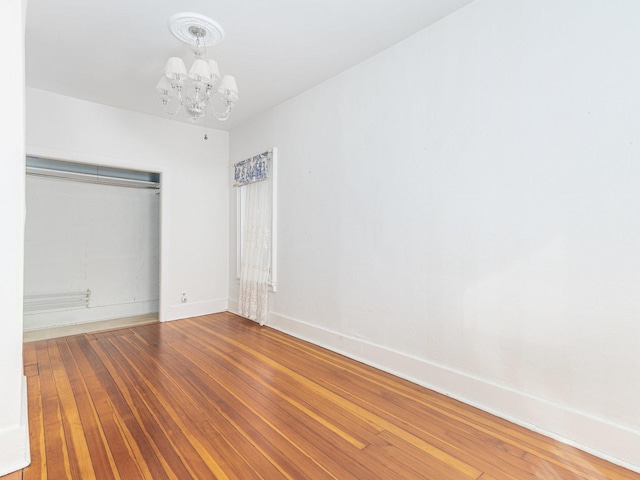 unfurnished bedroom featuring a chandelier, a closet, wood finished floors, and baseboards