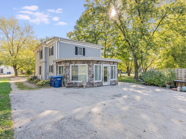 rear view of property with stone siding and central AC unit