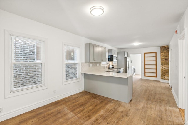 kitchen with tasteful backsplash, gray cabinets, kitchen peninsula, light wood-type flooring, and appliances with stainless steel finishes