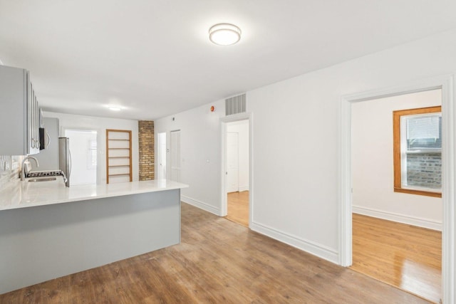 kitchen with sink, built in features, kitchen peninsula, stainless steel refrigerator, and light hardwood / wood-style flooring