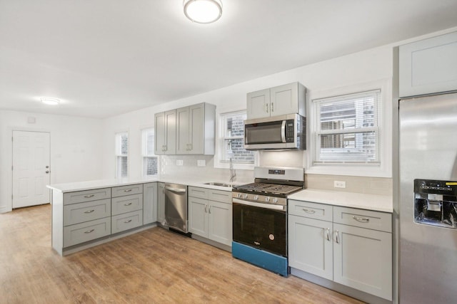 kitchen with kitchen peninsula, gray cabinets, stainless steel appliances, light hardwood / wood-style flooring, and sink