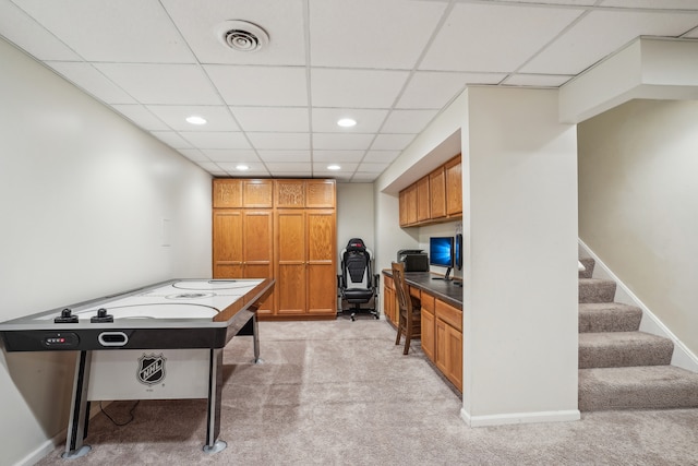 recreation room with light colored carpet, a drop ceiling, and built in desk