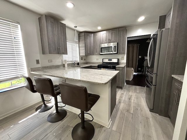 kitchen with kitchen peninsula, light wood-type flooring, a kitchen bar, pendant lighting, and stainless steel appliances