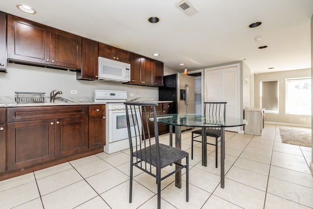 kitchen featuring dark brown cabinets, light stone counters, light tile patterned floors, and white appliances