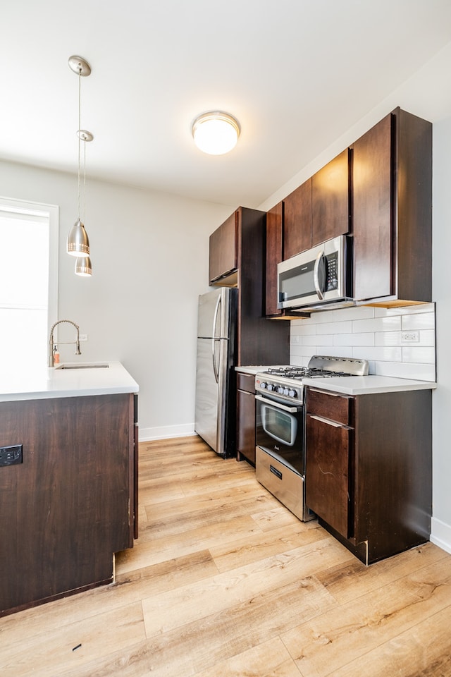 kitchen with appliances with stainless steel finishes, sink, light wood-type flooring, dark brown cabinets, and hanging light fixtures