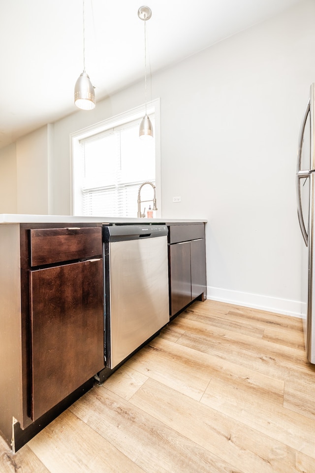 kitchen with stainless steel appliances, dark brown cabinetry, light hardwood / wood-style flooring, and decorative light fixtures