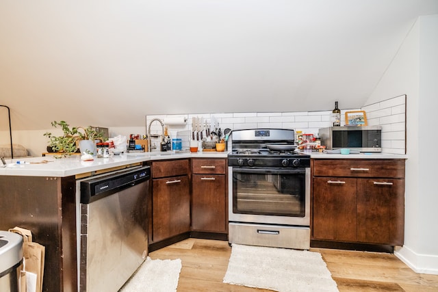 kitchen with kitchen peninsula, dark brown cabinets, light wood-type flooring, stainless steel appliances, and sink