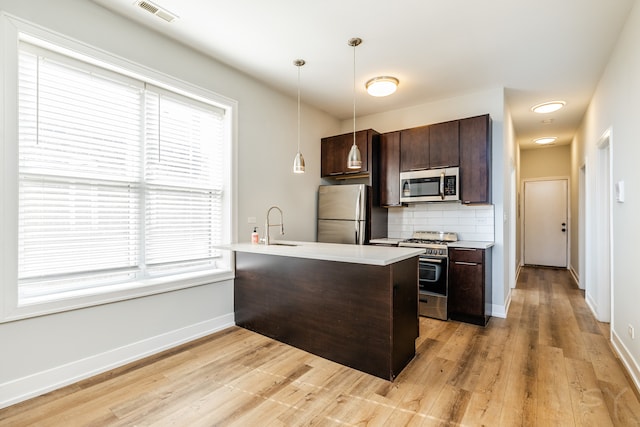 kitchen featuring decorative backsplash, hanging light fixtures, appliances with stainless steel finishes, light hardwood / wood-style flooring, and sink