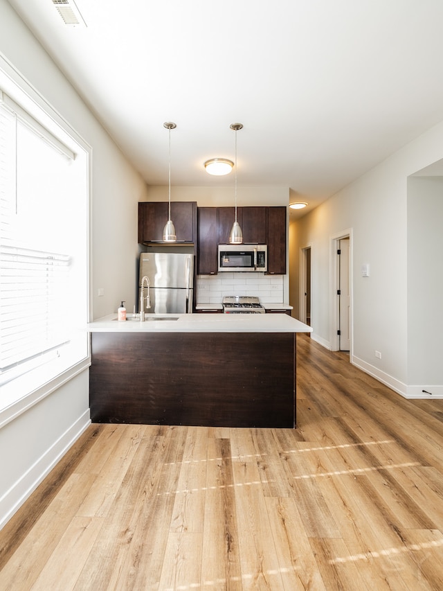 kitchen featuring light wood-type flooring, appliances with stainless steel finishes, pendant lighting, and backsplash