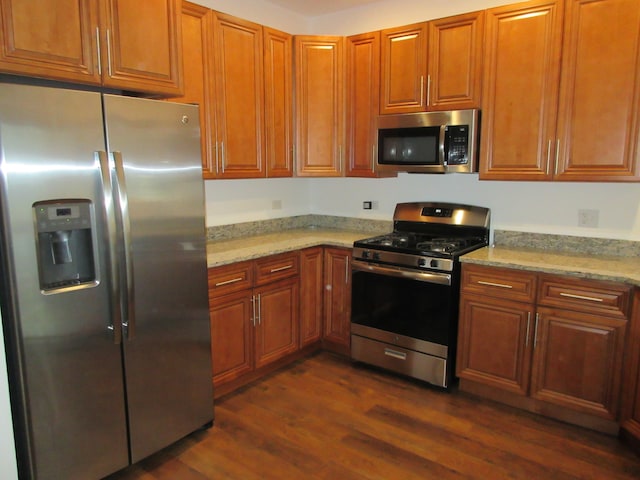 kitchen with appliances with stainless steel finishes, light stone counters, and dark wood-type flooring