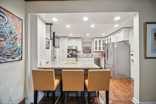 kitchen featuring white cabinetry, stainless steel appliances, a kitchen breakfast bar, dark hardwood / wood-style floors, and kitchen peninsula