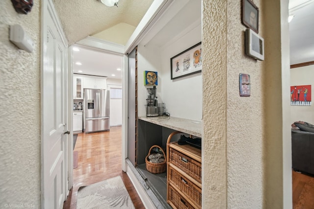 hallway featuring wood-type flooring, a textured ceiling, vaulted ceiling, and ornamental molding