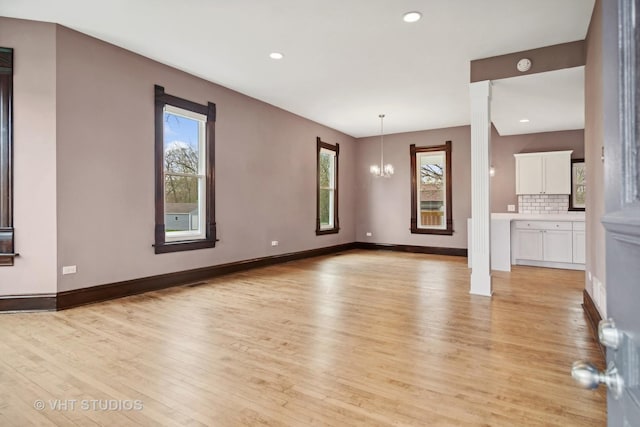 unfurnished living room featuring light hardwood / wood-style floors, an inviting chandelier, and a wealth of natural light