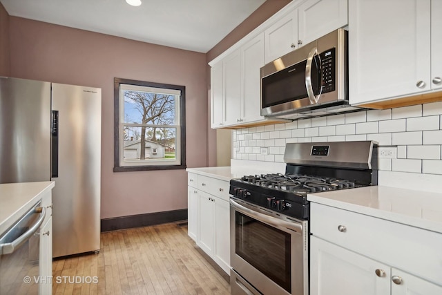 kitchen with tasteful backsplash, white cabinets, stainless steel appliances, and light hardwood / wood-style floors