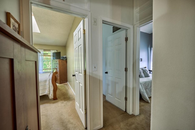 corridor featuring a textured ceiling, light colored carpet, and vaulted ceiling