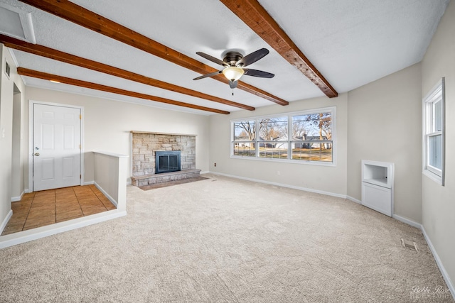 unfurnished living room featuring ceiling fan, a textured ceiling, a fireplace, beam ceiling, and light colored carpet