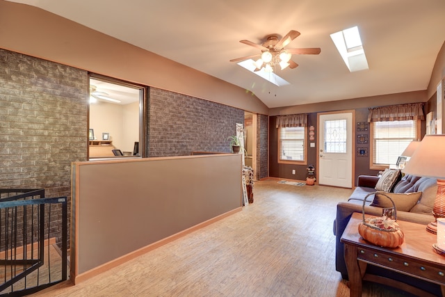 living room featuring lofted ceiling with skylight, brick wall, light hardwood / wood-style floors, and ceiling fan