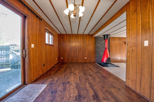 spare room featuring a wood stove, wooden walls, dark hardwood / wood-style flooring, and a notable chandelier