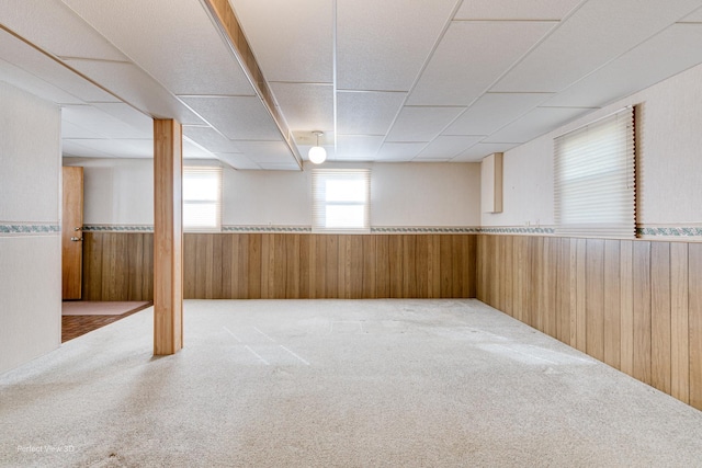 below grade area featuring carpet floors, wainscoting, wooden walls, and a drop ceiling