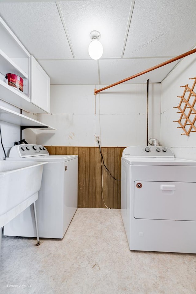 clothes washing area featuring a sink, laundry area, wood walls, and washing machine and clothes dryer