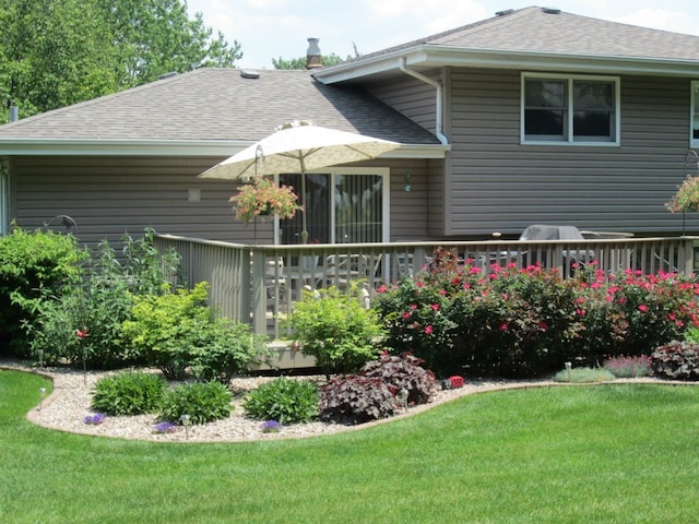 rear view of house with roof with shingles, a lawn, and a wooden deck