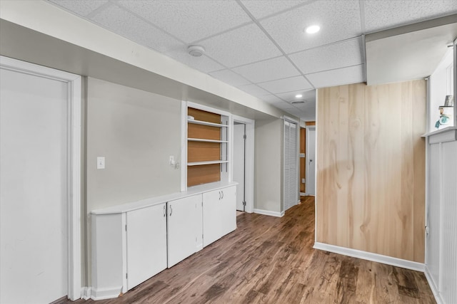 interior space featuring a drop ceiling, white cabinets, and wood-type flooring