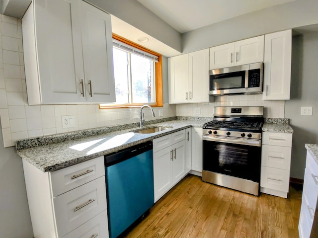 kitchen featuring appliances with stainless steel finishes, tasteful backsplash, sink, light hardwood / wood-style flooring, and white cabinets