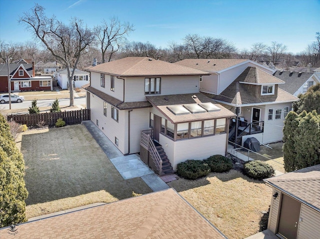 back of house with fence, a sunroom, a shingled roof, stairs, and a residential view