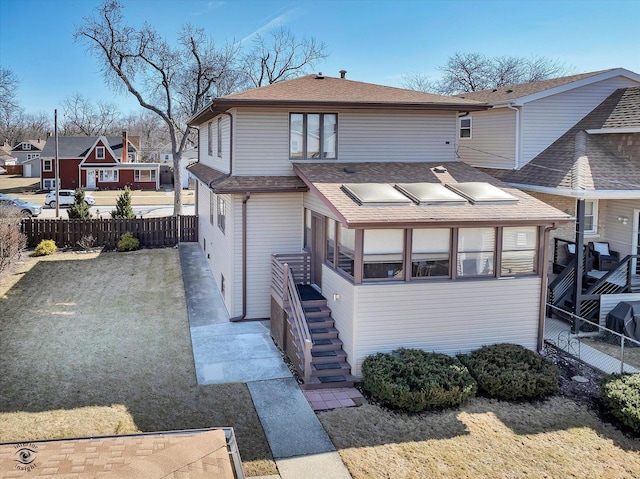 rear view of house with a lawn, a shingled roof, a sunroom, and fence