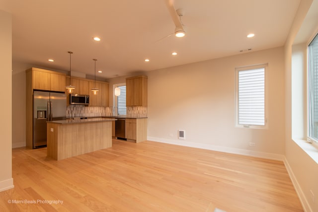 kitchen with tasteful backsplash, a kitchen island, stainless steel appliances, light hardwood / wood-style floors, and decorative light fixtures