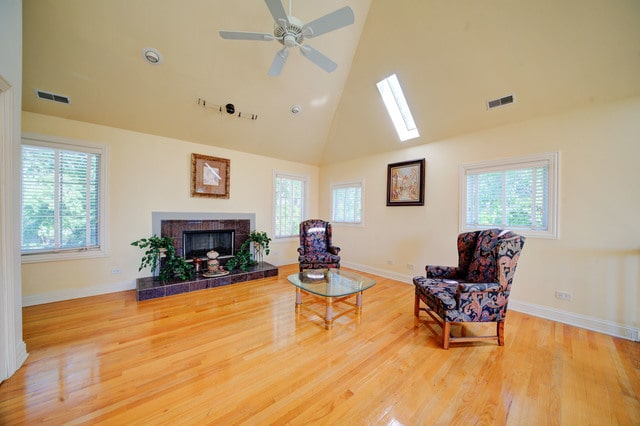 living area with a skylight, a fireplace, hardwood / wood-style floors, ceiling fan, and high vaulted ceiling