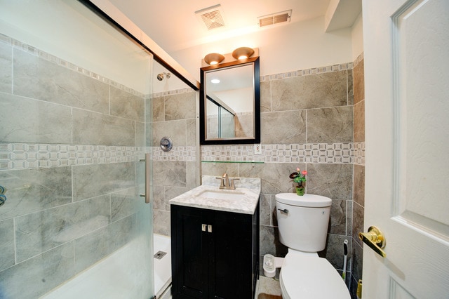 bathroom with vanity, toilet, tile walls, and a shower with shower door