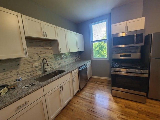 kitchen featuring light stone countertops, appliances with stainless steel finishes, sink, light wood-type flooring, and white cabinetry