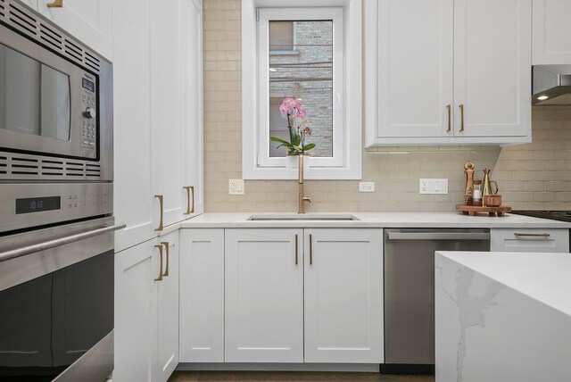 kitchen with tasteful backsplash, wall chimney range hood, sink, white cabinetry, and stainless steel appliances