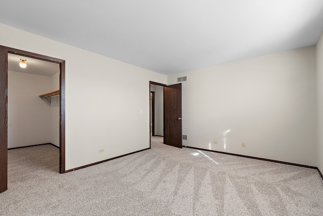 unfurnished bedroom with a walk in closet, a closet, and light colored carpet