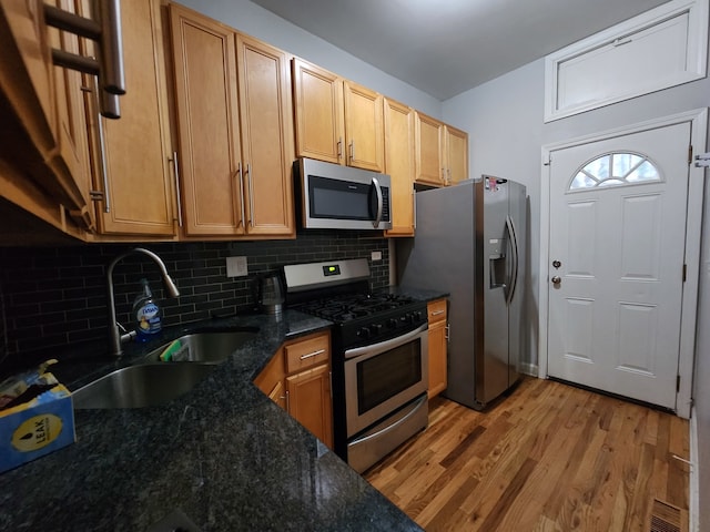 kitchen featuring decorative backsplash, appliances with stainless steel finishes, dark stone counters, light hardwood / wood-style flooring, and sink