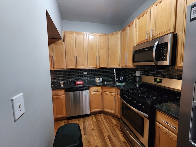 kitchen with sink, backsplash, stainless steel appliances, dark stone countertops, and light hardwood / wood-style flooring