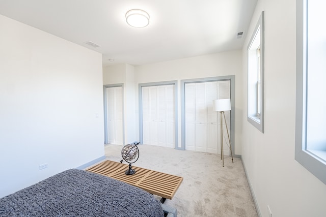 unfurnished bedroom featuring light carpet and multiple closets