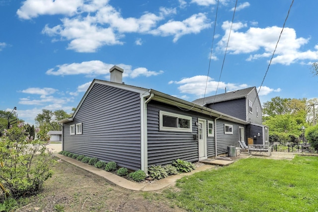 view of side of home featuring a chimney, a yard, and a patio area