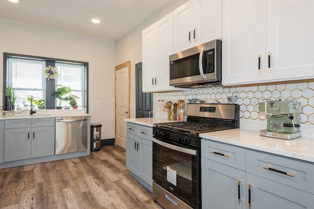 kitchen with backsplash, white cabinetry, light wood-type flooring, gray cabinets, and stainless steel appliances