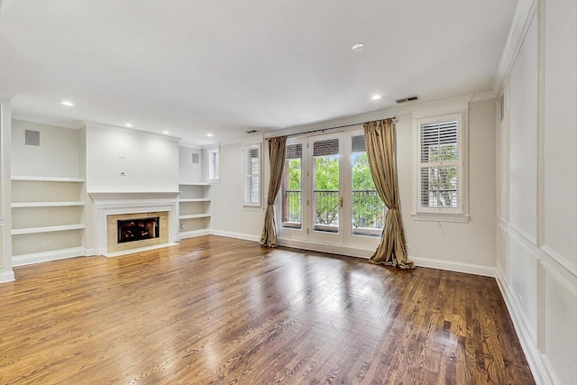 unfurnished living room with ornamental molding, built in features, a tiled fireplace, and wood-type flooring