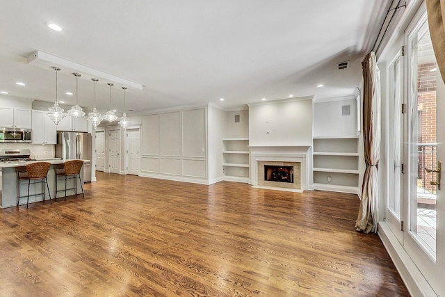 living room featuring ornamental molding, hardwood / wood-style floors, a tile fireplace, and built in shelves