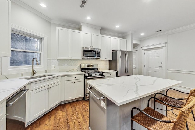 kitchen with light stone countertops, appliances with stainless steel finishes, sink, a center island, and a breakfast bar area