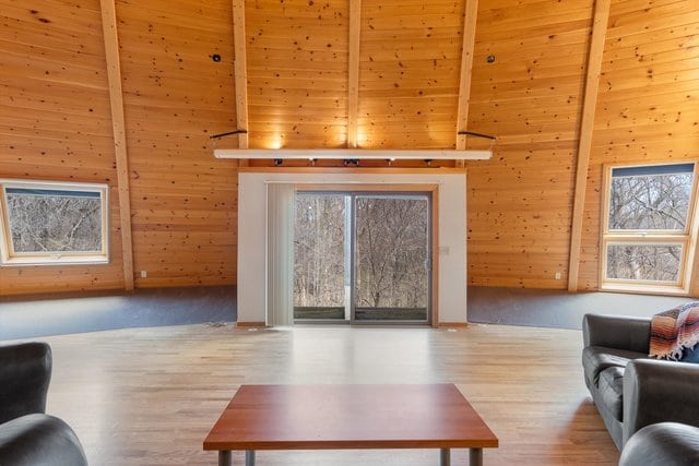 living room with beam ceiling, wood walls, light hardwood / wood-style flooring, and plenty of natural light