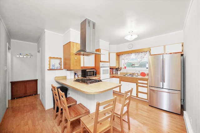 kitchen featuring kitchen peninsula, appliances with stainless steel finishes, a kitchen bar, range hood, and light hardwood / wood-style floors