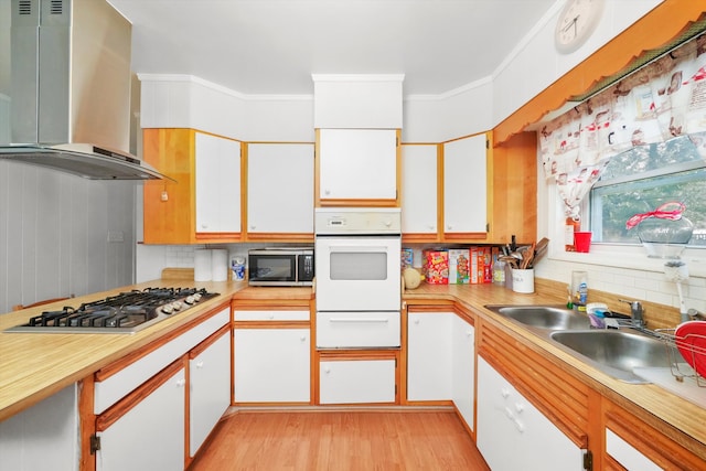 kitchen featuring stainless steel appliances, wall chimney range hood, decorative backsplash, and white cabinets