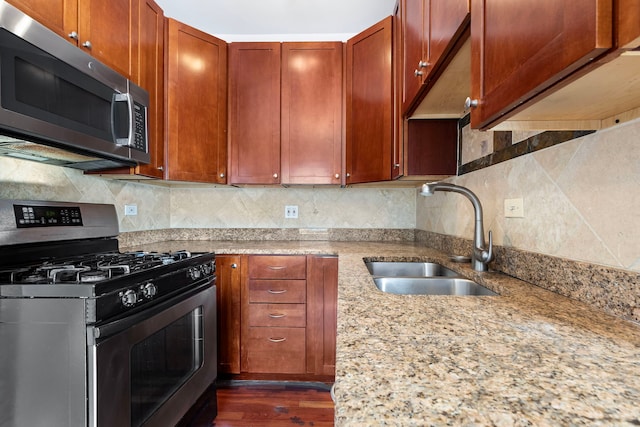 kitchen with sink, dark hardwood / wood-style flooring, stainless steel appliances, light stone counters, and decorative backsplash