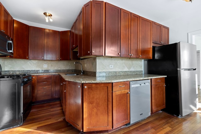 kitchen with stainless steel appliances, sink, light stone countertops, dark hardwood / wood-style flooring, and tasteful backsplash