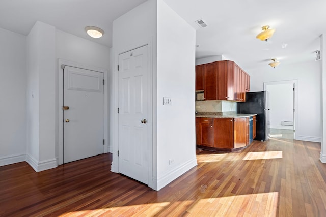 kitchen featuring baseboard heating, decorative backsplash, black refrigerator, and dark hardwood / wood-style flooring