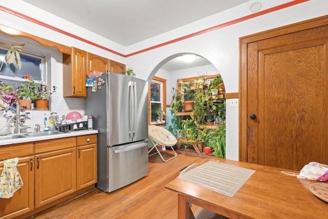 kitchen featuring tasteful backsplash, sink, light wood-type flooring, and stainless steel refrigerator